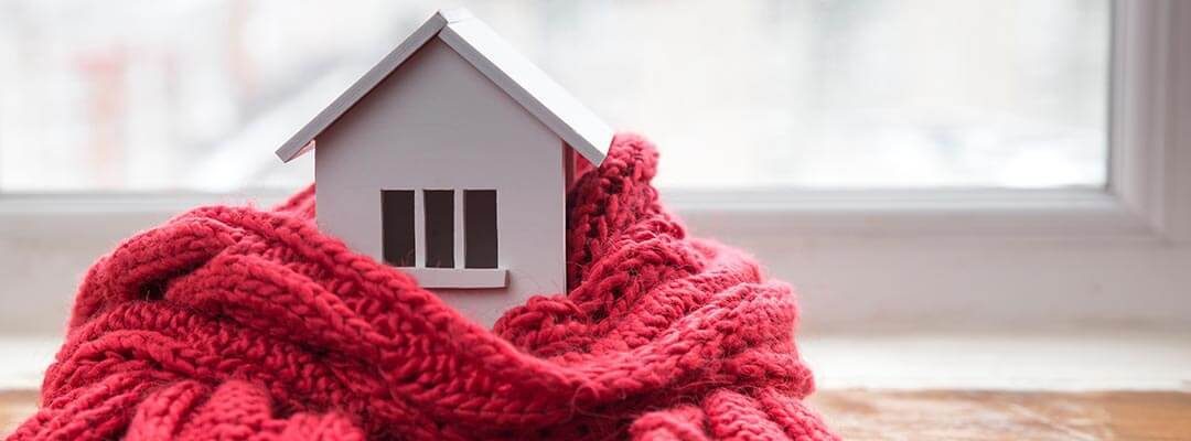 house in winter - heating system concept and cold snowy weather with model of a house wearing a knitted cap