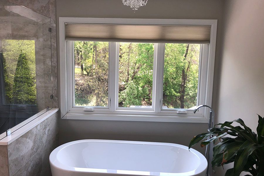 A beautiful residential bathroom with a large freestanding tub and three vinyl windows that were installed by professionals in the Quad Cities area.