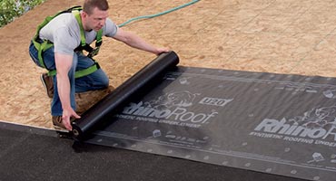 A home improvement expert installing RhinoRoof synthetic underlayment on a residential home in the Quad Cities area.