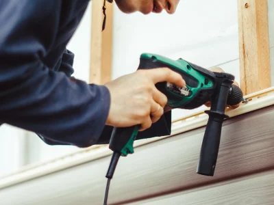 A person using a nail gun installing vinyl siding onto the side of a home located in the Quad Cities.