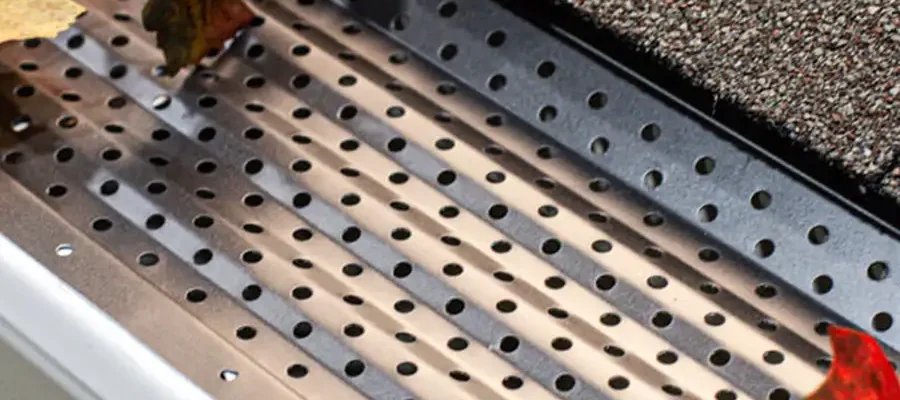 A close-up of a gutter guard covered with perforated metal and collecting autumn leaves from the roof.