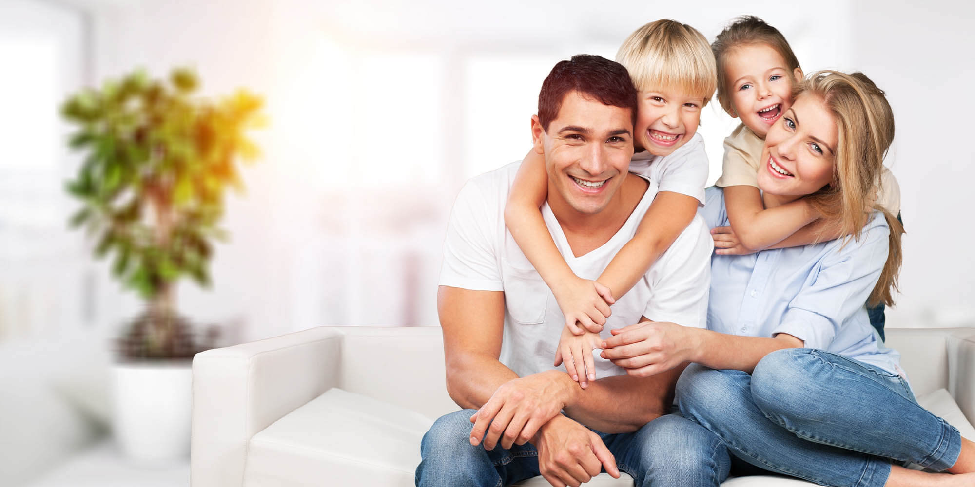 A smiling couple, seated on a couch, holds two children who are embracing them from behind. Despite the emergency caused by storm damage outside, the room remains bright with a blurred background and a potted plant.