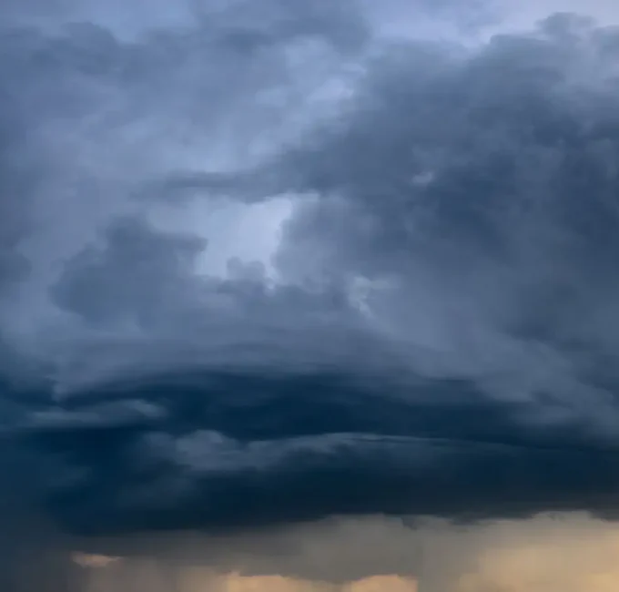 Dark, dense storm clouds dominate the sky, hinting at the potential for storm damage, with a faint light breaking through at the horizon.