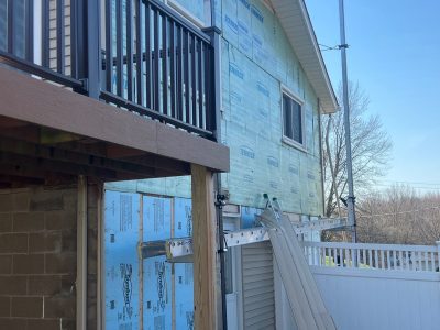 taylor ridge siding installation - backyard corner view of house with new siding layers and large brown deck, during